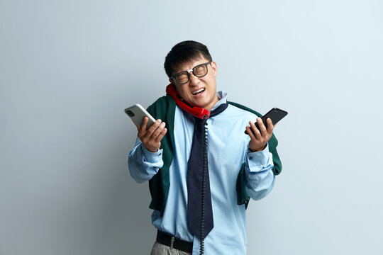 Nervous Man Answering Calls Isolated. Asian Businessman With Many Phones Feeling Stressful. Guy Talking Cellphone at Gray Background 