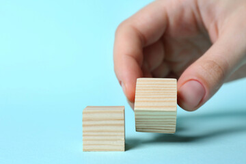 Woman arranging cubes on light blue background, closeup. Idea concept