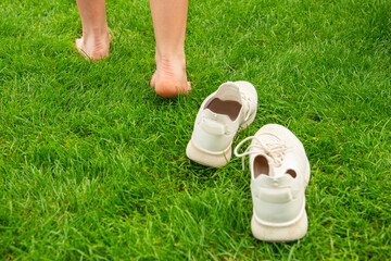 Woman leaving her sneakers and walking away barefoot on green grass, closeup