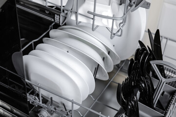Open modern dishwasher with clean tableware, closeup