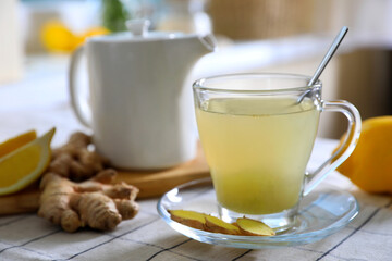 Glass of aromatic ginger tea and ingredients on white checkered tablecloth indoors, closeup. Space for text