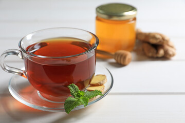 Cup of delicious ginger tea and ingredients on white wooden table, closeup. Space for text