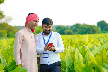 Young indian banker or officer showing some detail to farmer in smartphone at agriculture field