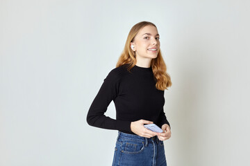 a happy woman with a phone and headphones smiles broadly standing on a white background