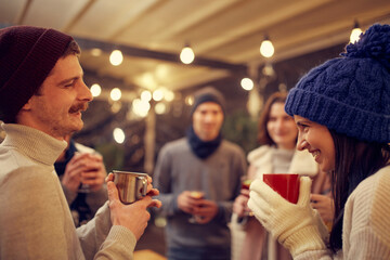 Happy smiling friends with cups of mulled wine having fun, spending time together at winter fair at...