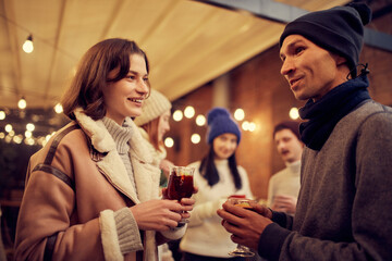 Happy couple in love in romantic dating with hot drinks, enjoying themselves, dressing warmly, looking at each other and smiling.