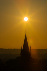 An autumn sunrise in Maastricht with in silhouette the tower of the church of Sint Pieter with the sun aligned above the religious Christian cross