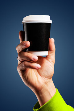 Male hand holds, raised black paper cup of tea or coffee.
