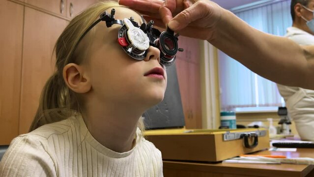 ophthalmologist diagnoses a little girl's vision on a sign projector and makes a selection of lenses. phoropter. trying on lenses for glasses. astigmatism diagnosis at optometrist. close up