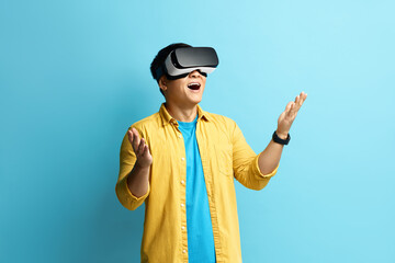 Focused Man Trying VR. Portrait of Amazed Asian Guy Discovering New Technologies Wearing Virtual Reality Headset, Futuristic 3d Vision. Indoor Studio Shot Isolated on Blue Background 