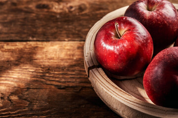 Red apples in a wooden bowl on an old wooden table top.