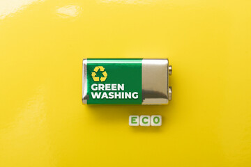 Greenwashing concept: battery on yellow background and die composing the word eco