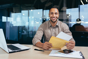 Portrait of happy african american man in office doing paperwork, man looking at camera and smiling...