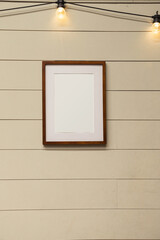 Blank wooden picture frame on vintage plank wall with light bulbs over it