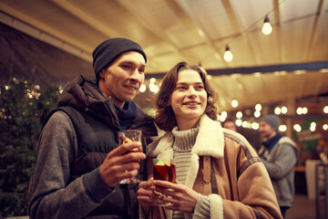 Happy couple in love in romantic dating with hot drinks, enjoying themselves, dressing warmly, looking at each other and smiling.