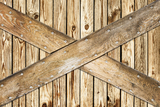 Wooden barn door. X shape wooden desks. Rustic nails vintage desk construction background. Countryside architecture texture. Village building farm door entrance.