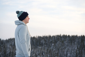 Fototapeta na wymiar Handsome guy, young relaxed man is breathing deep deeply fresh air outdoors at winter snowy cold frosty day standing on top peak of mountain in forest on natural background. Copy space, place for text
