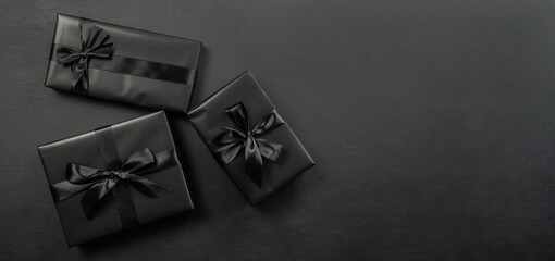 Gift box wrapped in black paper with a black bow on a dark background.Holiday concept. Black...