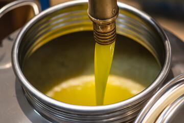 Fresh extra virgin olive oil pouring into tank at a cold-press factory after the olive season harvesting, vertical