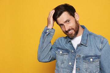 Bearded man fixing hair on orange background. Space for text