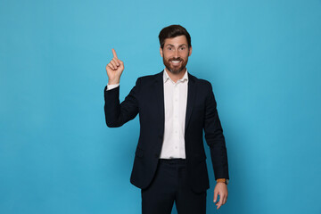 Smiling bearded man pointing index finger up on light blue background