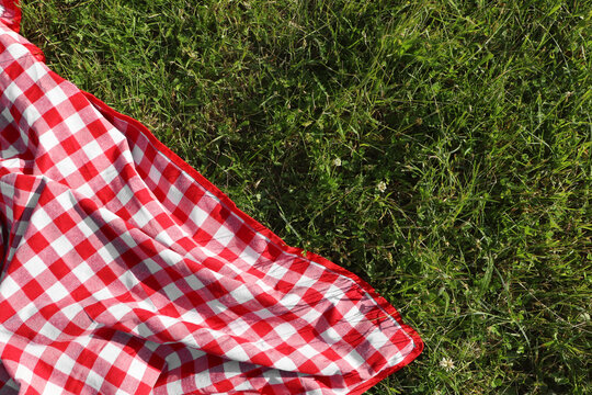 Checkered picnic tablecloth on fresh green grass, top view. Space for text - Powered by Adobe