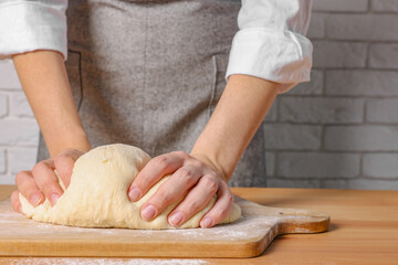 Woman kneading dough at wooden table near white brick wall, closeup