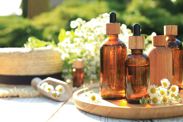 Bottles of essential oil and flowers on white wooden table outdoors, space for text