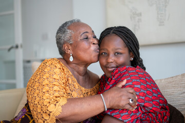 Smiling senior woman hugging and kissing teenage granddaughter at home
