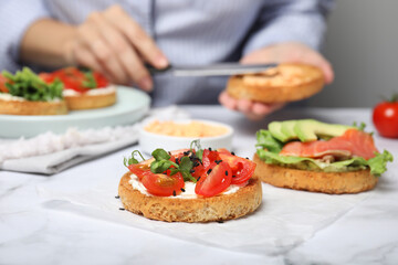 Woman making tasty rusks with different toppings at white marble table, closeup