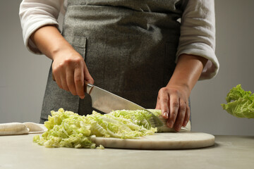 Woman cutting fresh Chinese cabbage at light grey table, closeup