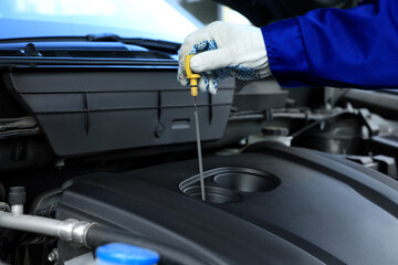 Worker checking motor oil level in car with dipstick, closeup - obrazy, fototapety, plakaty