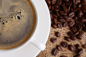 Cup of hot aromatic coffee and roasted beans on sackcloth, flat lay. Space for text