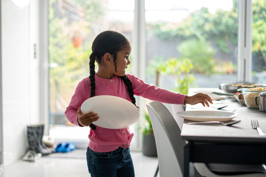 Girl placing dishes on dining table