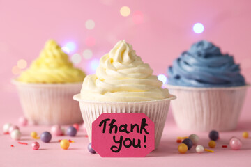 Tasty cupcakes and note with phrase Thank You on pale pink background