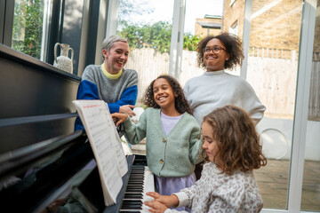 Smiling woman and daughters assisting girl playing piano at home © Cultura Creative