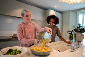 Smiling woman pouring pasta into bowl in kitchen