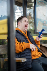 Fototapeta na wymiar Man sitting on bench at bus stop, using smart phone