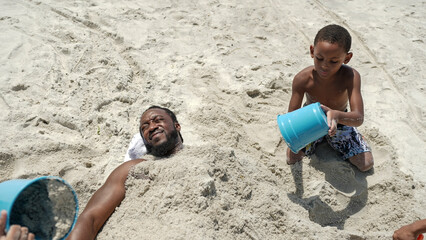 USA, Boy covering father with sand on beach