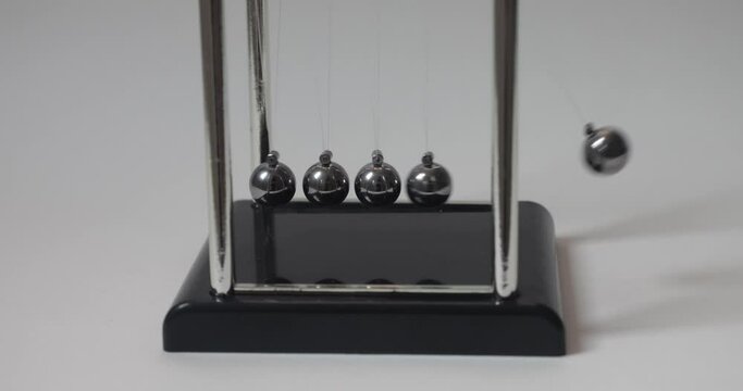 Newton's cradle. Kinetic pendulum against white background. Chromatic metal balls wobble and slow down. Moving something, inertia concept, science, physics lesson. Psychological hypnosis session