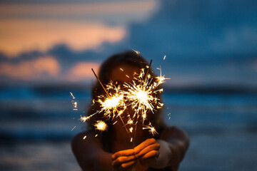 Woman with sparklers on the beach at sunset