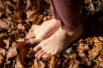Close-up of bare feet of woman standing on dried leaves - obrazy, fototapety, plakaty