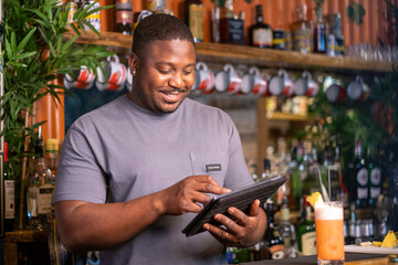 Smiling bartender using tablet at bar