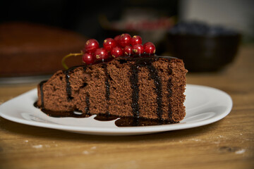 Handmade chocolate cake decorated with cranberries and red currants on the wooden kitchen table.