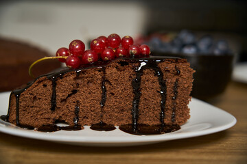 Handmade chocolate cake decorated with cranberries and red currants on the wooden kitchen table.