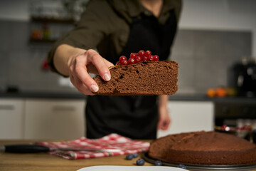 Woman with a passion for cooking decorates a slice of handmade chocolate cake in her home kitchen with blackberries and red currants.