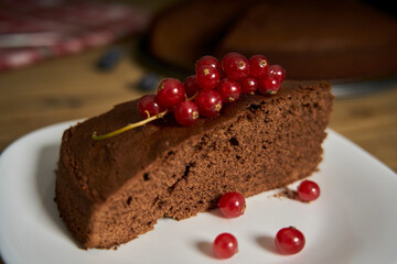 Handmade chocolate cake decorated with cranberries and red currants on the wooden kitchen table.