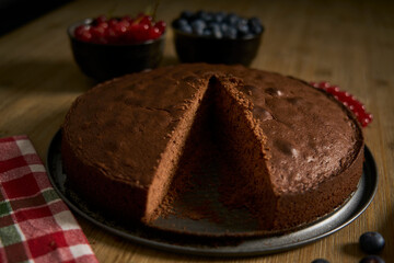 Handmade chocolate cake decorated with cranberries and red currants on the wooden kitchen table.