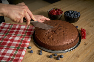 Woman with a passion for cooking decorates a slice of handmade chocolate cake in her home kitchen with blackberries and red currants.