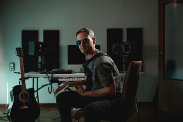 Guitarist and music producer posing with his electric guitar on his lap during a recording at his...